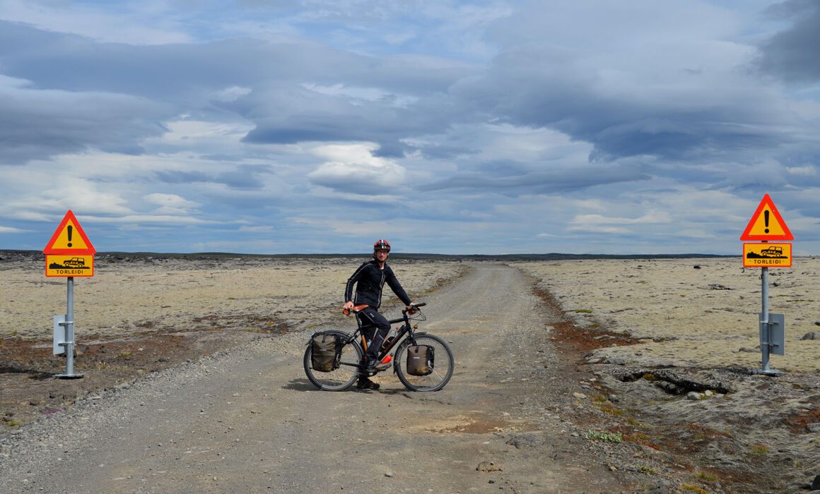 Fietser op een Santos reisfiets op een onverharde hooglandweg in IJsland, tussen twee verkeersborden die het traject als alleen begaanbaar voor 4x4-voertuigen markeren